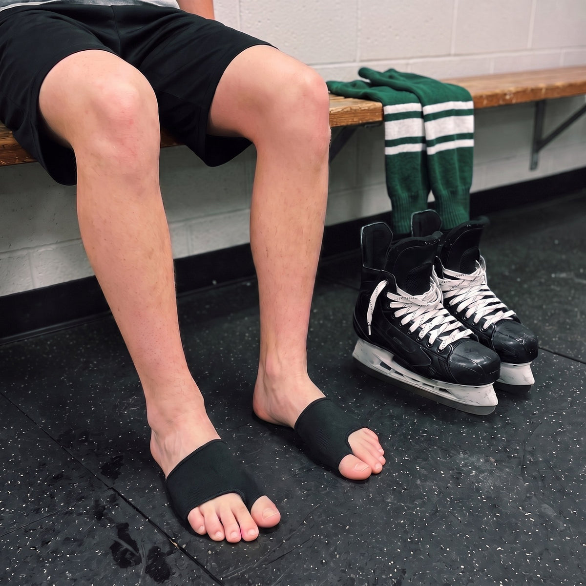 Hockey player on a dressing room bench with an Olyra Blister Sleeve on each foot