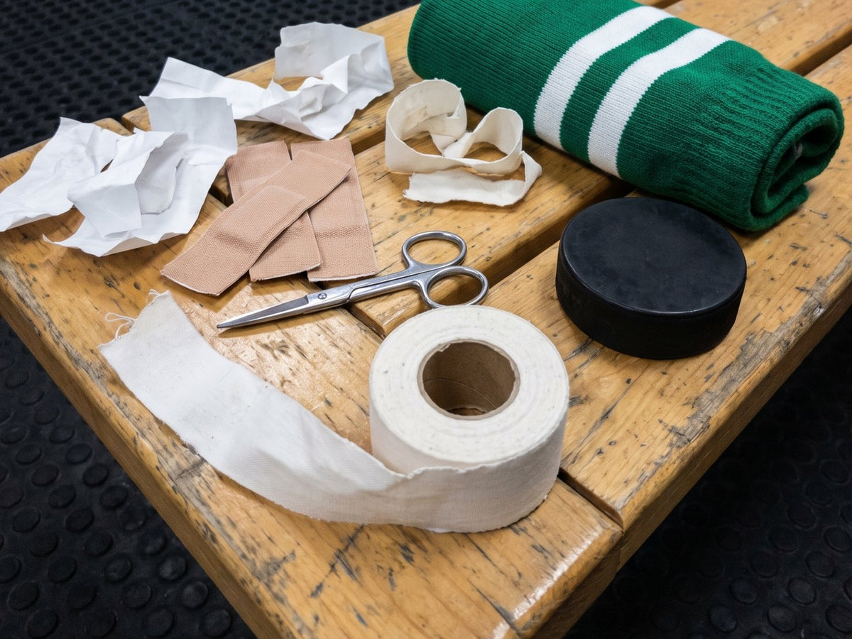 Athletic tape, Band-Aids and scissors on a dressing room bench next to a hockey sock and a puck