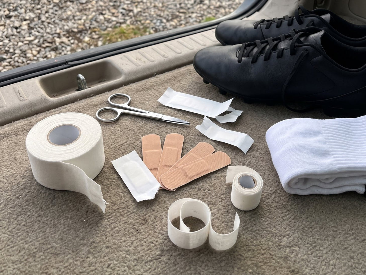 Athletic tape, Band-Aids and scissors laid out next to soccer cleats and a pair of socks