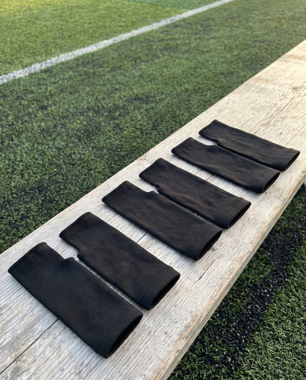 Six Olyra Blister Sleeves, three pairs, laid out on a bench beside a soccer field